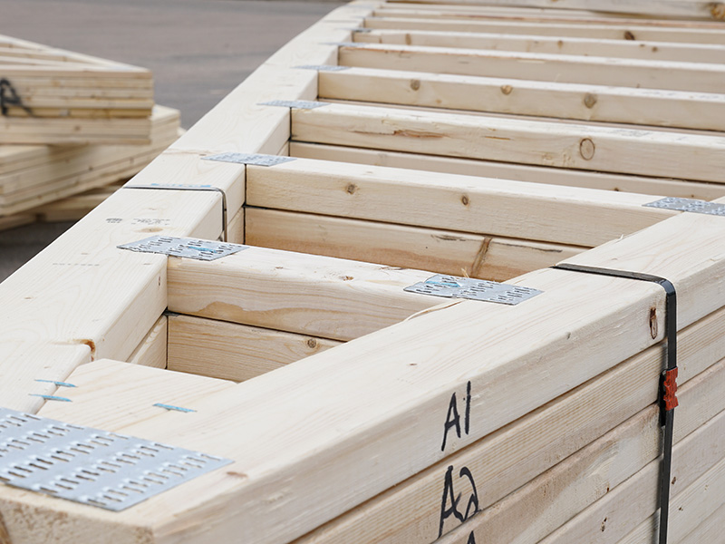 Stack of prefabricated wooden roof trusses with metal plates, ready for delivery from a component manufacturing facility.
